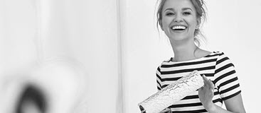 Young woman smiles holding a paint roller in her new home. The First Home Buyers Deposit scheme gives eligible members the chance to own a home sooner.